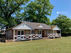 Sports pavilion with wide veranda set in the trees under a blue sky