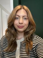 Woman with light brown hair, wearing black and white cardigan